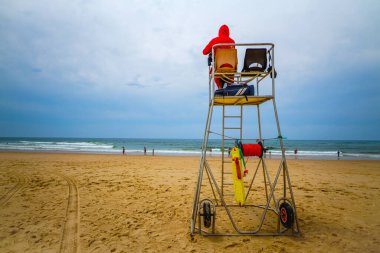 ARCACHON, FRANCE- 18 HAZİRAN 2019: Gözetleme kulesinde oturan cankurtaran Fransız plajında denize doğru bakıyor ve tatillerde ve yaz aylarında ufukta turist ve insanlarla deniz kıyısına bakıyor.