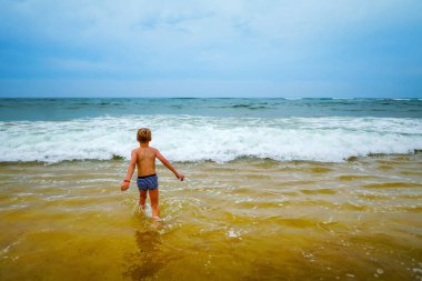 Neşeli çocuk tatillerde soğuk deniz suyuna giriyor. Neşeli ve neşeli çocuk sahilde eğleniyor. 