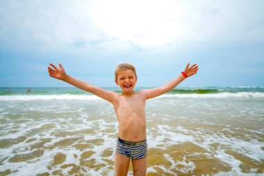 Arkasında dalgalar ve deniz olan neşeli bir çocuk. Neşeli ve neşeli çocuk deniz kıyısında eğleniyor. 