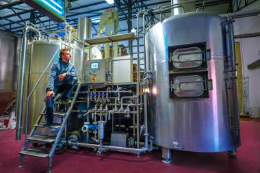 HERON, BELGIUM - NOVEMBER 9, 2019: Belgian craft beer Leopold 7 tanks and barrels with employee in brewery clipart
