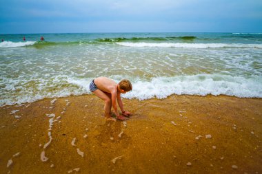 Neşeli çocuk tatillerde soğuk deniz suyuna giriyor. Neşeli ve neşeli çocuk sahilde eğleniyor. 