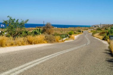 Yol, bitki, deniz ve mavi gökyüzüyle güneşli bir manzara. 