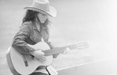Genç bir kadın sahilde gitar çalıyor.