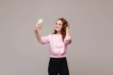 Beyaz bir arka planda izole edilmiş akıllı telefondan selfie çeken çekici bir kadının portresi.