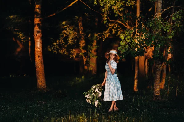 Piękna dziewczyna ciesząca się zapachem lilii w letni dzień. Aromaterapia i wiosenna koncepcja. Ładna dziewczyna, piękna kobieta w niebieskiej, długiej, vintage sukience stoi w liliowym ogrodzie. Ogrodnictwo — Zdjęcie stockowe