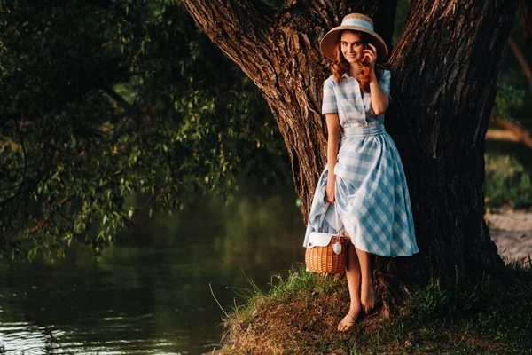Mladá krásná dívka v slaměném klobouku a se slaměným sáčkem má výhled na jezero — Stock fotografie