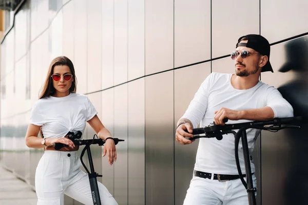 Ein Mädchen und ein Mann laufen auf Elektrorollern durch die Stadt, ein verliebtes Paar auf Motorrollern. — Stockfoto