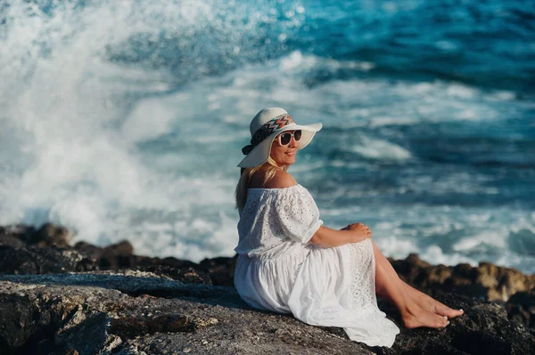 Flicka sitter på stranden av Atlanten i en vit klänning och en halmhatt — Stockfoto