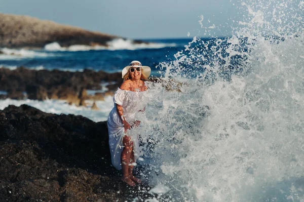 Une belle fille en robe blanche et un chapeau de paille se tient sur le rivage sous les grands boeufs de l'océan Atlantique. Grandes vagues près de ses jambes . — Photo