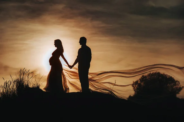 Homem amoroso abraça uma mulher grávida ao pôr do sol, contra o pano de fundo do mar, rio, de pé no cais. Retrato de belos recém-casados esperando um bebê. Fotografia, conceito — Fotografia de Stock