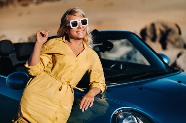 Çöl vadisinde yolculuktan zevk alan genç bir kadının hayat tarzı portresi, yol kenarındaki üstü açık arabadan iniyor.