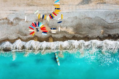 Güzel bir çift Fransa sahilinde sörf tahtalarının yanında yatıyor, bir kuadkopterden ateş ediyorlar, bir sürü sörf tahtası sahilde alışılmadık bir şekilde yatıyor.