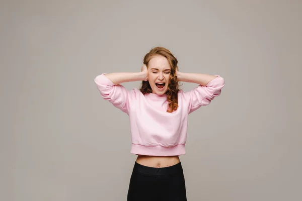 Una hermosa chica sobre un fondo gris sostiene su cabeza y grita emocionalmente — Foto de Stock