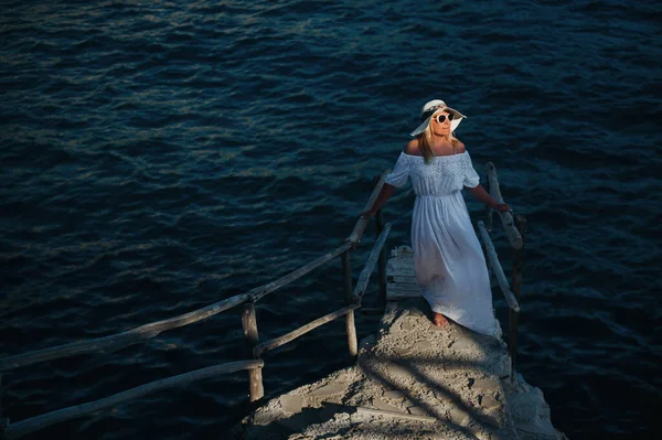 Una bella ragazza in abito bianco si trova sul molo vicino al mare.Woman in Grecia vicino al mare al tramonto — Foto Stock