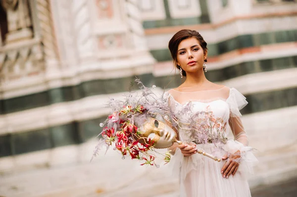 Наречена з прекрасним квітковим візерунком, як маска у Флоренції, стильна наречена у весільній сукні, що стоїть з масками у Старому місті Флоренції. Модель у Флоренції — стокове фото