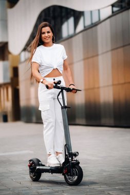 Beyaz elbiseli güzel bir kız şehirde elektrikli scooter kullanıyor..