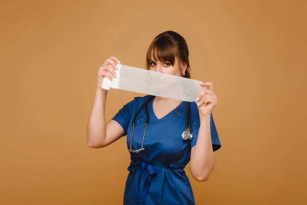 medic woman in white coat and mask holds a twisted gauze bandage for dressing wounds, white background.