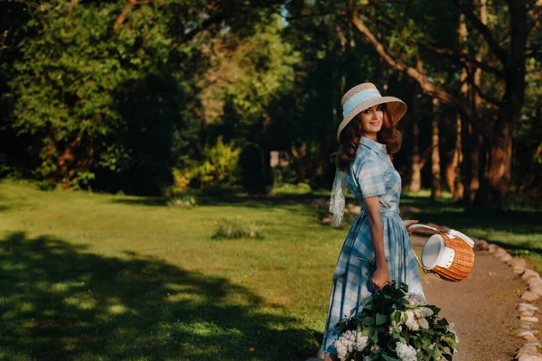 在阳光明媚的春天 一个戴着草帽的年轻貌美的姑娘站在公园里 手里拿着一束盛开的白花紫丁香 — 图库照片