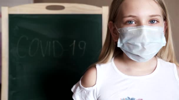 A little girl at home wears a medical mask, behind which is the inscription COVID-19.Removes the mask — Stock Video