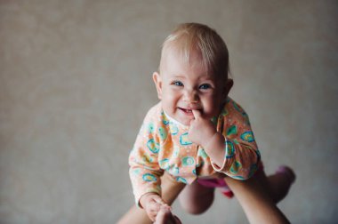 Annesinin kollarında, ağzında bir parmağıyla gülümseyen küçük bir kız..