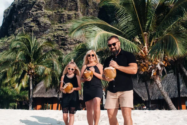 Una familia elegante en ropa negra con cocos en sus manos en la playa de la isla de Mauricio. Hermosa familia en la isla de Mauricio en el océano Índico — Foto de Stock