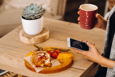 Bir kız masada oturuyor ve bir kafede akıllı telefonuyla mesajlaşıyor. Bir kız elinde telefonuyla bir kafede oturuyor. Telefona yazıyor..