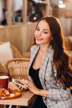 Bir kız masada oturuyor ve bir kafede akıllı telefonuyla mesajlaşıyor. Bir kız elinde telefonuyla bir kafede oturuyor. Telefona yazıyor..