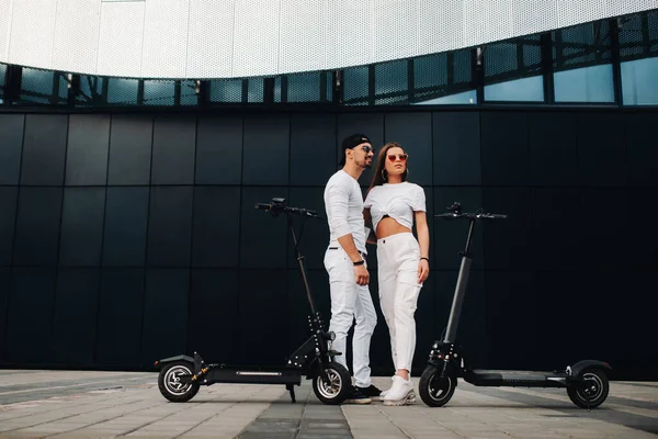 A girl and a guy are walking on electric scooters around the city, a couple in love on scooters