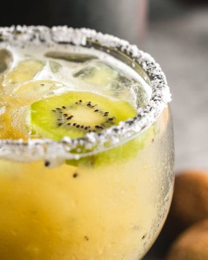 Kivi margaritası, büyük margarita bardağında, jant buzunda tuz dilimlenmiş kivi, kivi ve gri yüzey.