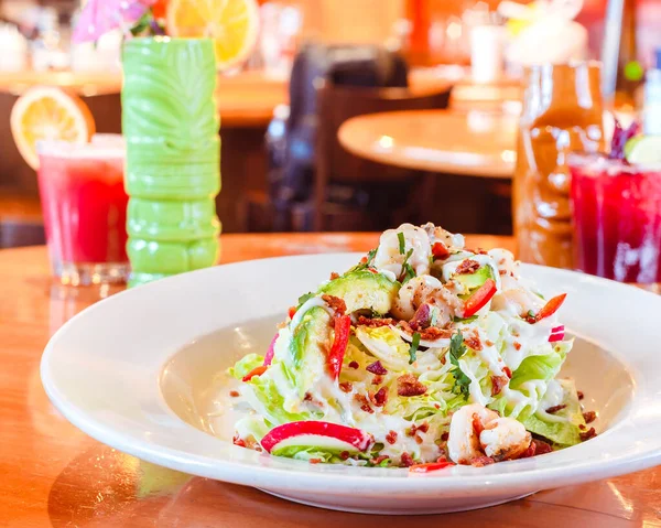 Tasty traditional mexican salad with dressing and red pepper on a light brown wood shiny surface in a traditional mexican restaurant surrounded by traditional mexican drinks
