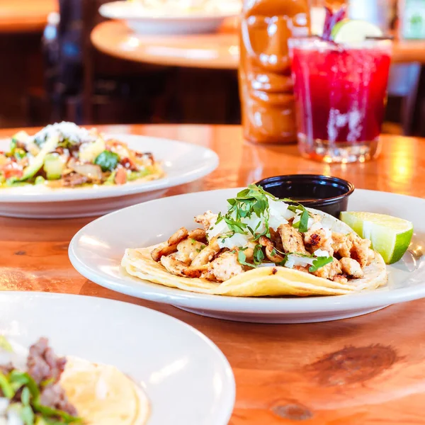 Taco platter at a traditional mexican restaurant surrounded by other traditional mexican plates drinks and other restaurant tables