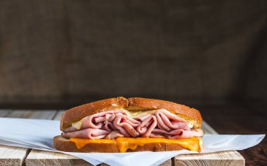 Kasap kağıdı ve ahşap yüzey üzerinde jambon ve erimiş peynirli sandviç.