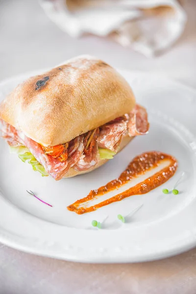 Beyaz bir tabağın üzerinde salamlı bir ciabatta.