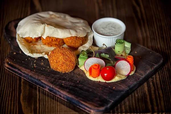 Tahta bir masanın tepesinde pide bir humus ve falafel.