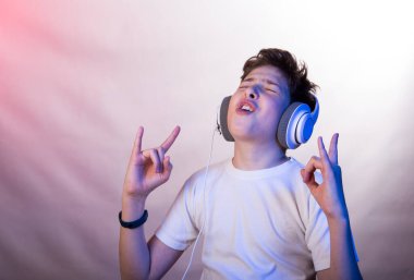 En sevdiği müziği dinleyen genç bir adamın duyguları ve neşesi. Beyaz tişörtlü, arka planda açık mor tonları olan genç bir adamın fotoğrafı.