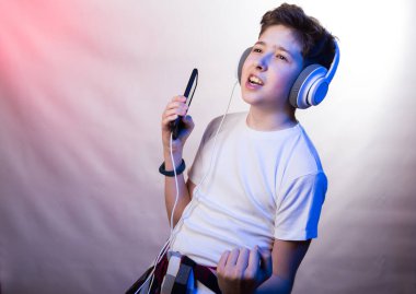 En sevdiği müziği kulaklıkla cep telefonu kullanarak dinleyen genç bir adamın duyguları ve zevki. Beyaz tişörtlü, arka planda açık mor tonları olan genç bir adamın fotoğrafı.