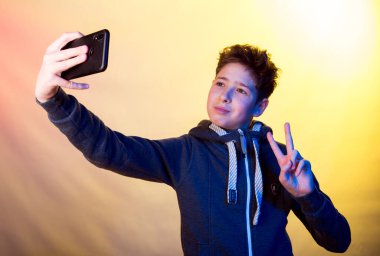 Cep telefonu kullanan genç bir adamın duyguları ve neşesi. Koyu renk spor ceketli genç bir adamın sarı gölgelerin arka planında fotoğrafı.