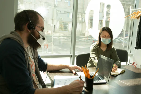 An online lesson during quarantine. Young teachers (man and woman) in medical masks conduct an online lesson.