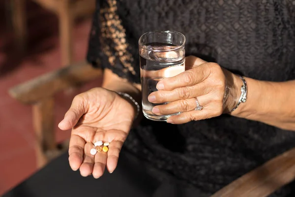 Femme âgée avec des pilules dans la main et un verre d'eau potable — Photo