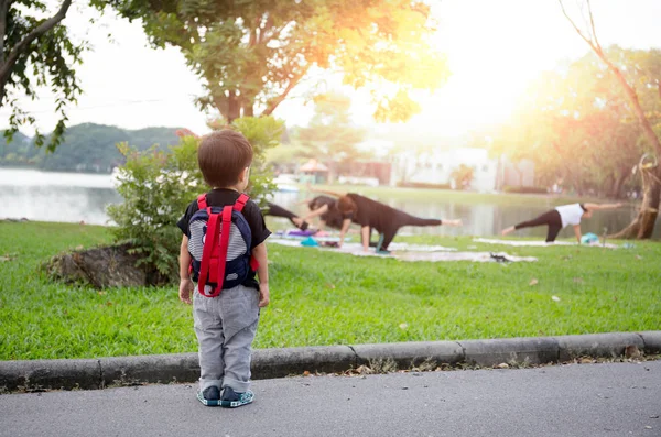 Um menino pequeno fora de pé assistindo mãe fazendo ioga — Fotografia de Stock
