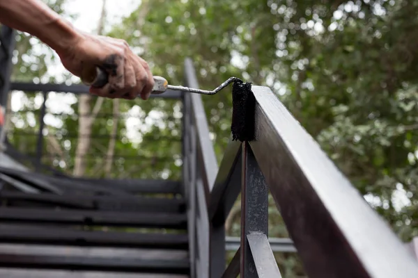 Tangan memegang rol cat menerapkan cat hitam di tangga logam — Stok Foto