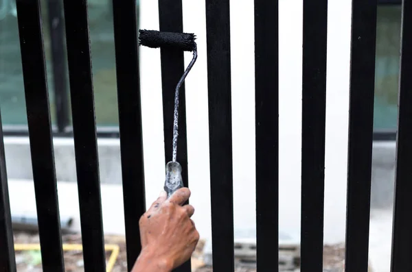 Hand holding paint roller applying black paint on the fence — Stock Photo, Image