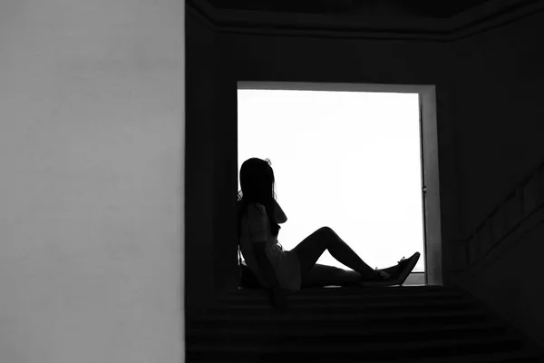 Silhouette teen girl sitting on door step thinking in black and — Stock Photo, Image