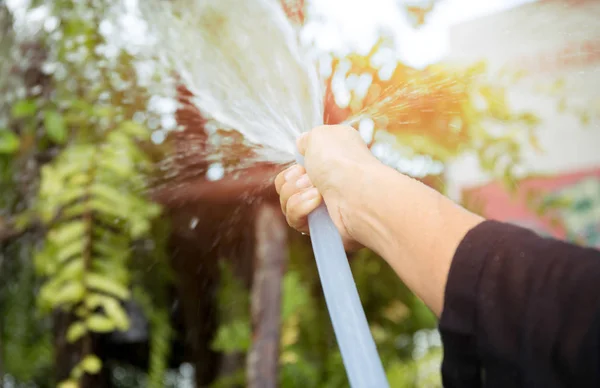 Mulher regando o jardim com água de mangueira de jardim — Fotografia de Stock