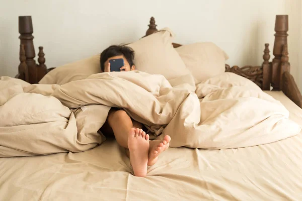 Ragazzino sdraiato su un letto a piedi nudi giocando al cellulare — Foto Stock
