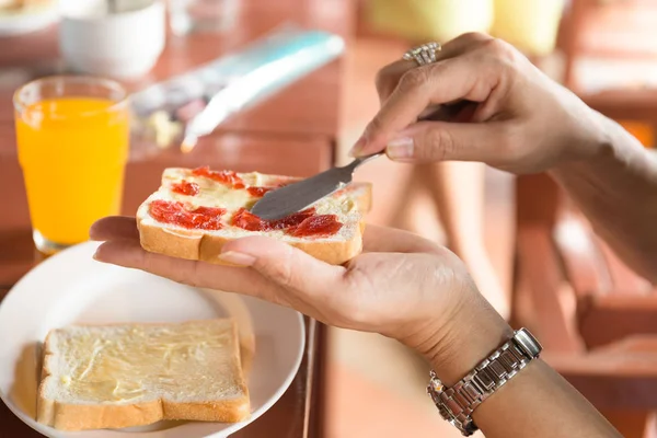 Breakfast with woman hand spreading strawberry jam on top slice — Stock Photo, Image