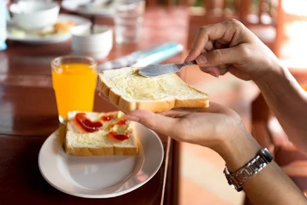 Frukost med kvinna hand sprider smör på skiva bröd och o — Stockfoto