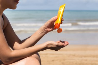 Kadın elleri güneş kremi şişesinden güneş kremi sürüyor.