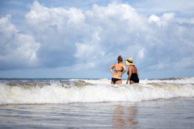 Anne ve kızı s büyük dalga ile oynarken bir mayo