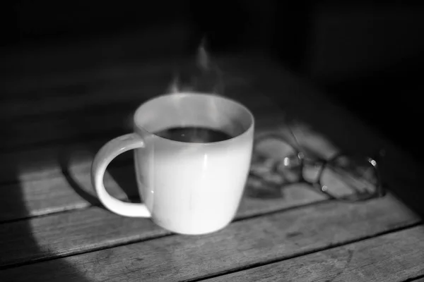 Taza de café blanco y negro y vasos sobre mesa de madera al sol —  Fotos de Stock